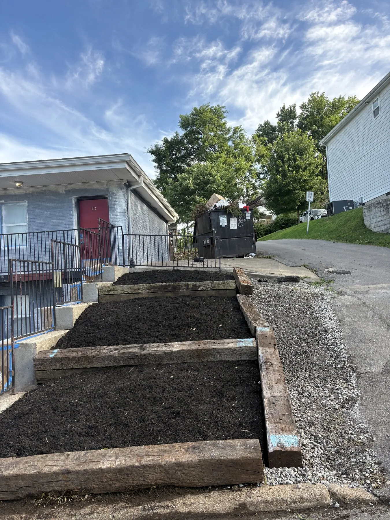 Terraced garden beds edged with railroad ties, filled with fresh soil beside a building