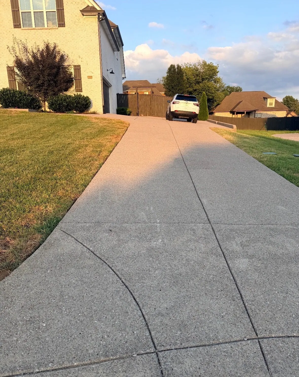 Long concrete driveway beside a cream brick home before sealing